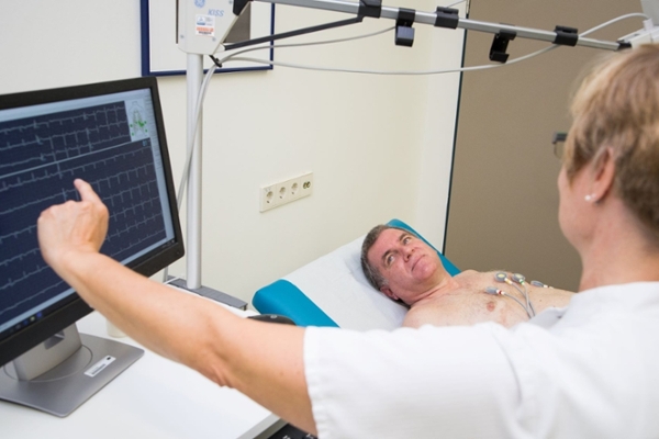 Mann auf Liege, Frau deutet auf einen Monitor Mann auf Liege, Frau deutet auf einen Monitor